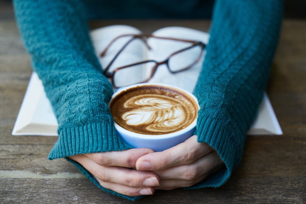 The Art of Hygge in Canada Woman wearing warm jumper clasps a mug of coffee in her hands