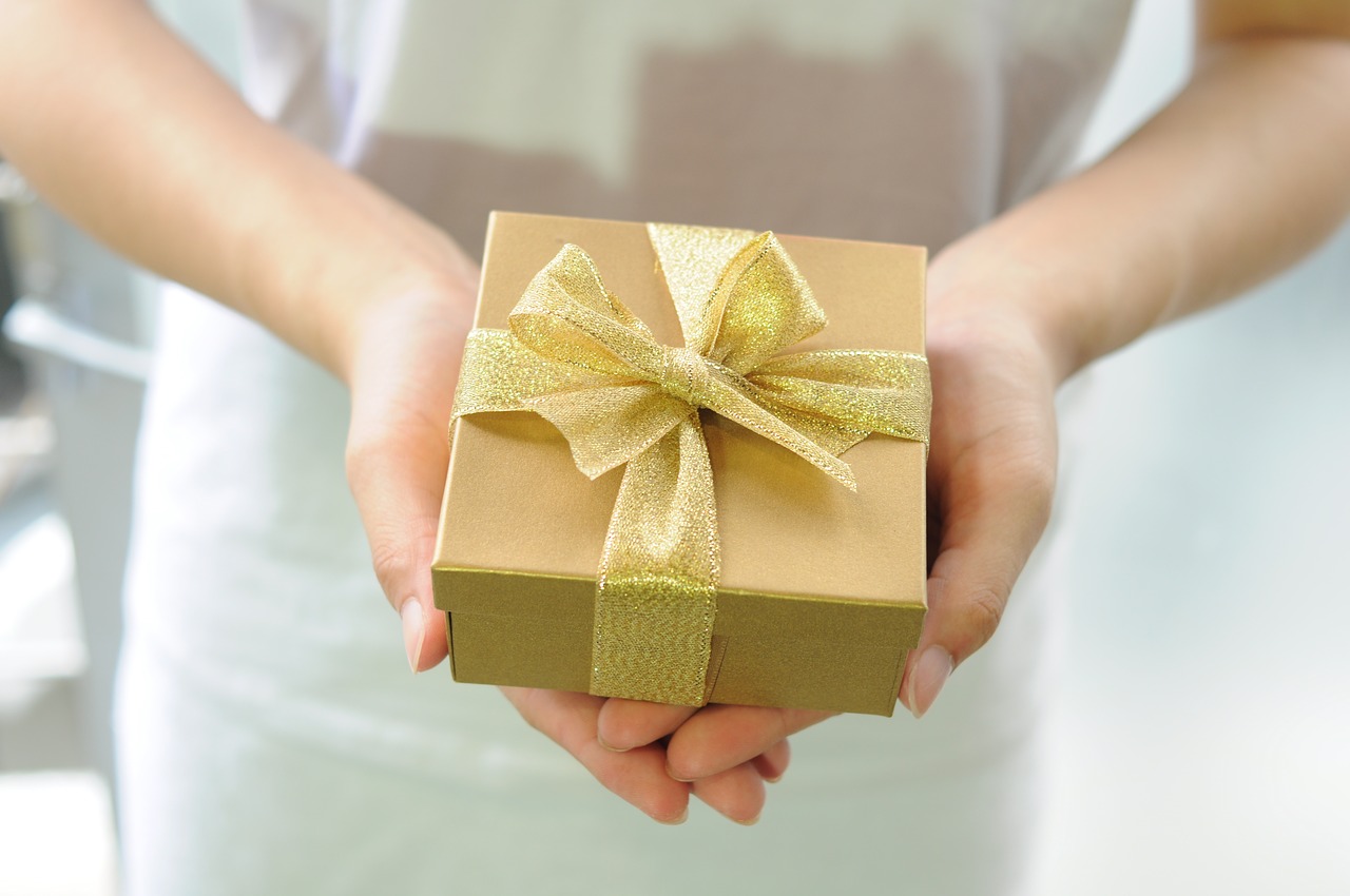 Generous Canadian Lottery Winners Woman holds a gold-wrapped gift in her outstretched hands.
