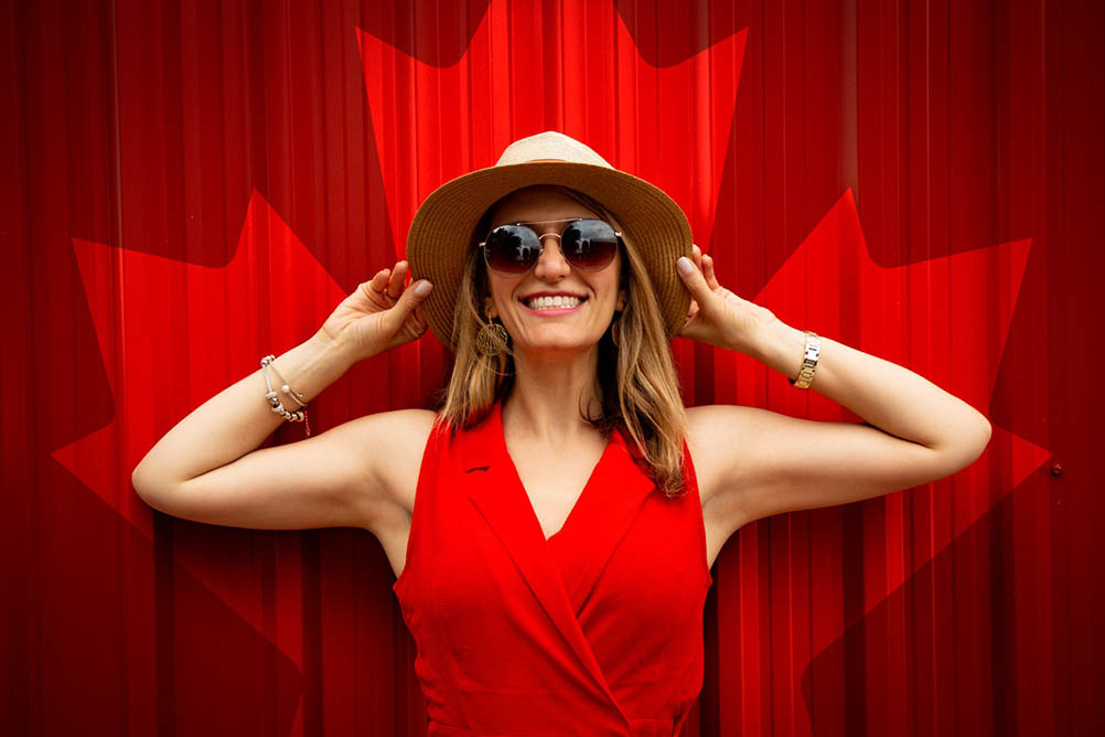 Woman in red smiles while standing in front of a Canadian maple leaf mural