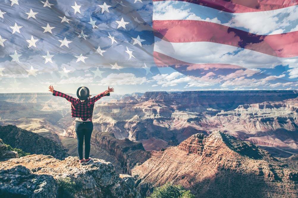 Man celebrates a lottery win on top of a mountain with American flag superimposed on the sky